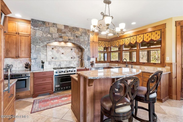 kitchen with a sink, stainless steel appliances, a notable chandelier, light stone countertops, and decorative backsplash