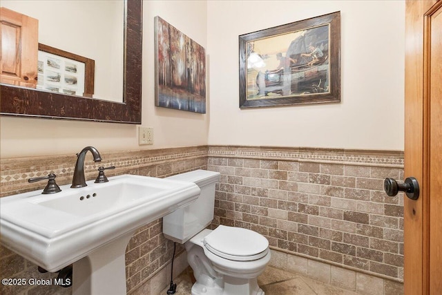 bathroom with wainscoting, toilet, a sink, and tile walls