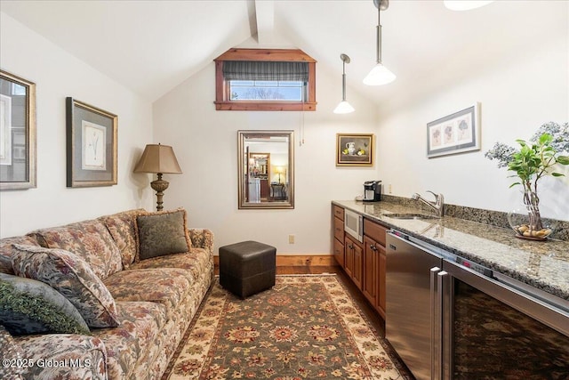 living room featuring light wood-style flooring, wet bar, baseboards, and vaulted ceiling with beams