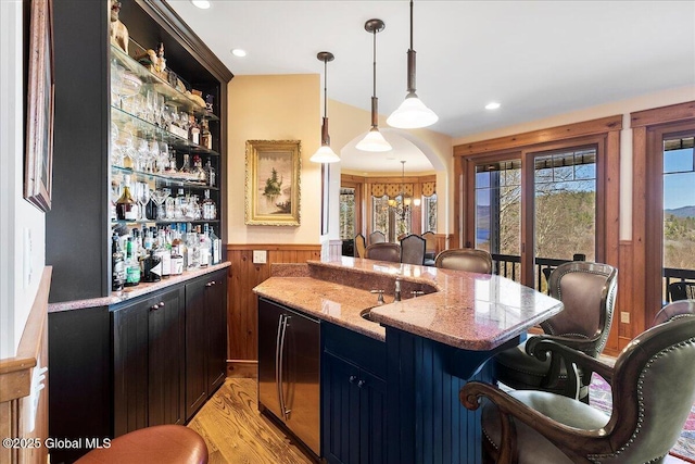 bar with a wainscoted wall, decorative light fixtures, indoor wet bar, and a healthy amount of sunlight