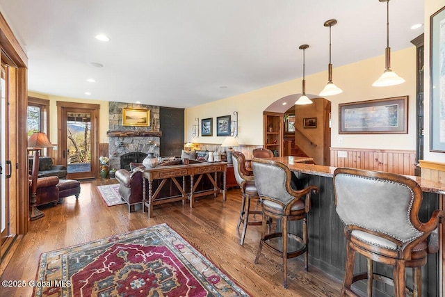 interior space with a bar, wood finished floors, wainscoting, and a stone fireplace