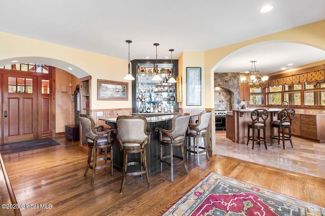bar with light wood finished floors, hanging light fixtures, arched walkways, and indoor bar