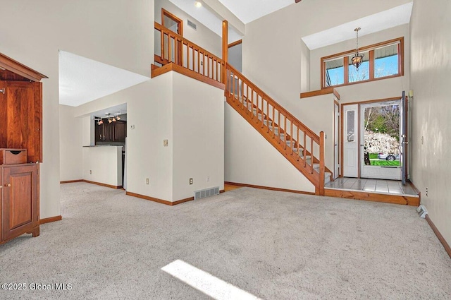 carpeted entrance foyer with visible vents, stairs, a towering ceiling, and baseboards