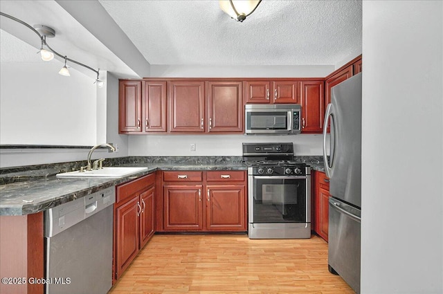 kitchen featuring dark countertops, a textured ceiling, a sink, light wood-style flooring, and stainless steel appliances