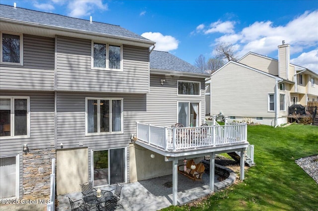 rear view of property with a yard, a deck, a patio area, and roof with shingles