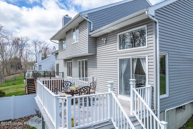 exterior space with fence, a deck, a chimney, stairs, and outdoor dining space
