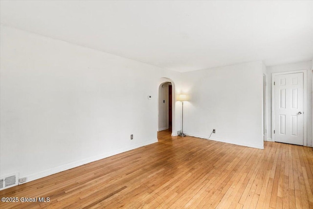 empty room featuring arched walkways, baseboards, light wood-type flooring, and visible vents