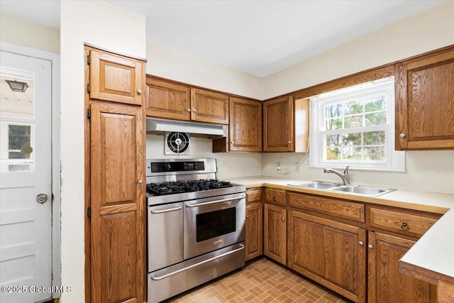kitchen featuring brown cabinets, a sink, gas stove, light countertops, and under cabinet range hood