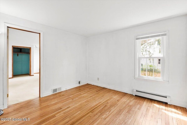 empty room with baseboards, a baseboard radiator, hardwood / wood-style flooring, and visible vents