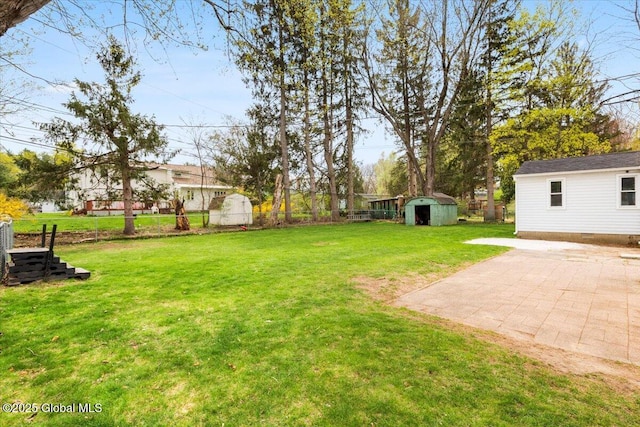 view of yard with fence, a storage unit, an outbuilding, and a patio