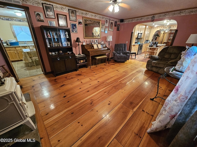 living room with arched walkways, ceiling fan, light wood finished floors, a textured ceiling, and crown molding