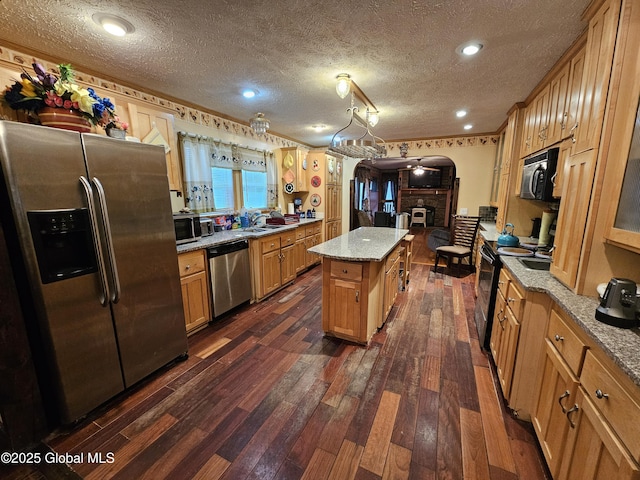 kitchen featuring a textured ceiling, a sink, appliances with stainless steel finishes, a center island, and dark wood-type flooring
