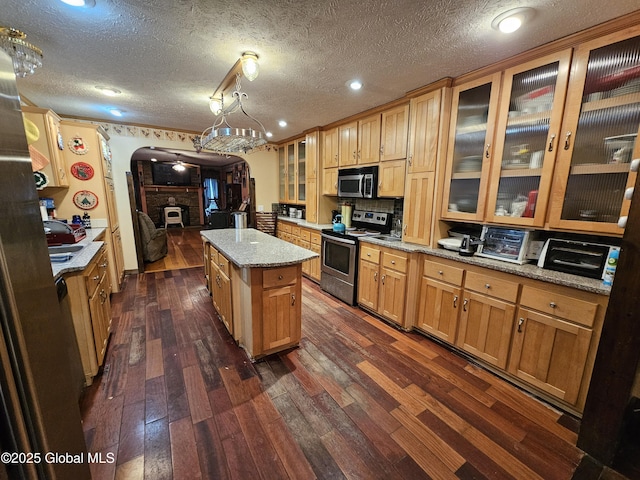 kitchen with a center island, light stone counters, arched walkways, appliances with stainless steel finishes, and dark wood finished floors