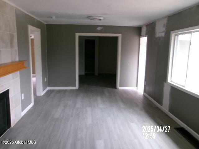 unfurnished living room with a tile fireplace, wood finished floors, and baseboards