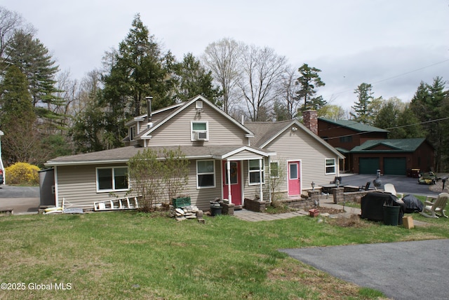view of front facade featuring an outdoor structure, a front lawn, driveway, and roof with shingles