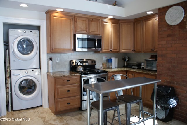 kitchen with appliances with stainless steel finishes, stacked washer and clothes dryer, a toaster, recessed lighting, and stone counters