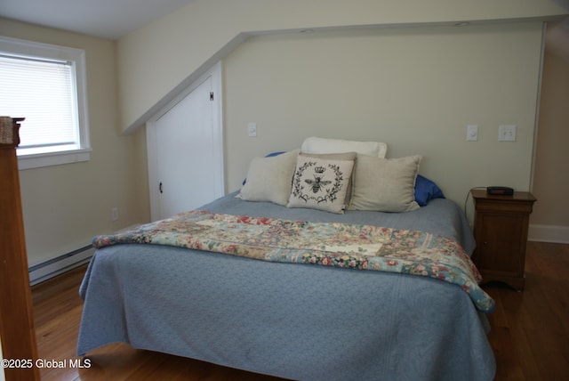 bedroom featuring baseboards, wood finished floors, and a baseboard heating unit
