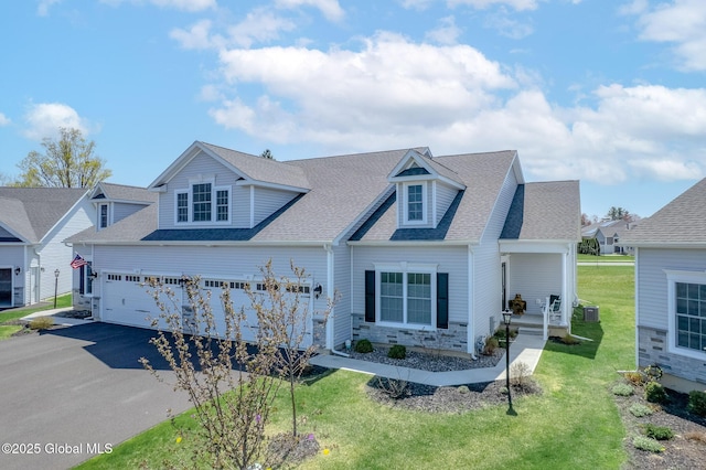 new england style home featuring a front lawn, covered porch, stone siding, roof with shingles, and driveway