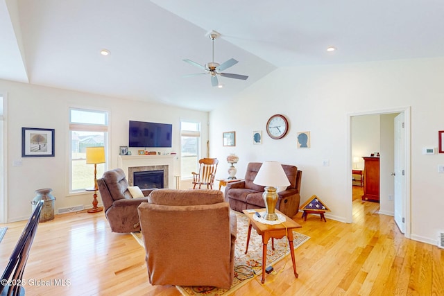 living area featuring visible vents, a glass covered fireplace, lofted ceiling, light wood-style floors, and ceiling fan