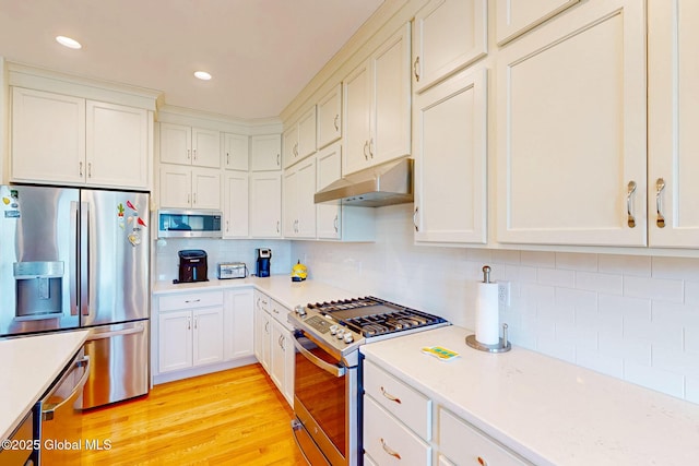 kitchen featuring tasteful backsplash, light countertops, under cabinet range hood, stainless steel appliances, and white cabinetry