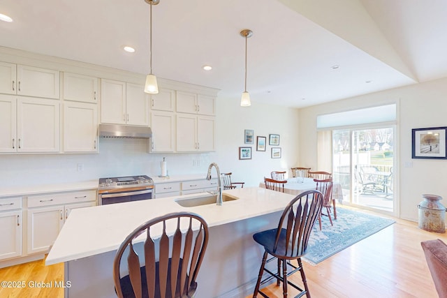 kitchen with stainless steel range with gas stovetop, a sink, light countertops, light wood finished floors, and under cabinet range hood