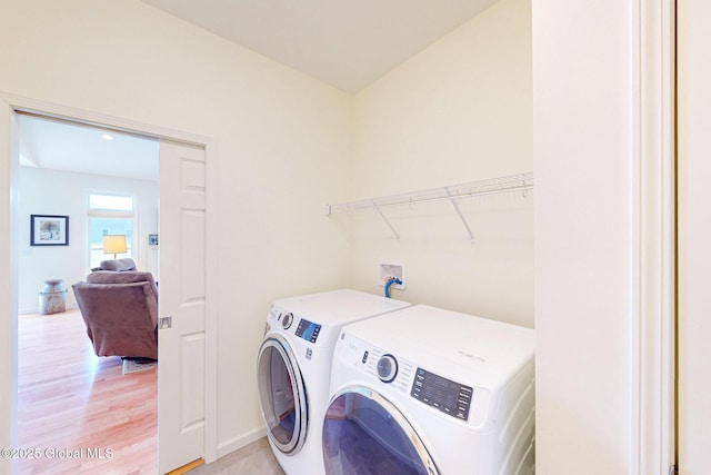 clothes washing area with washing machine and clothes dryer, laundry area, baseboards, and light wood-style floors