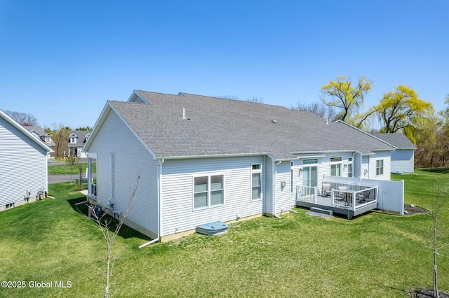 rear view of house with a yard, a deck, and roof with shingles