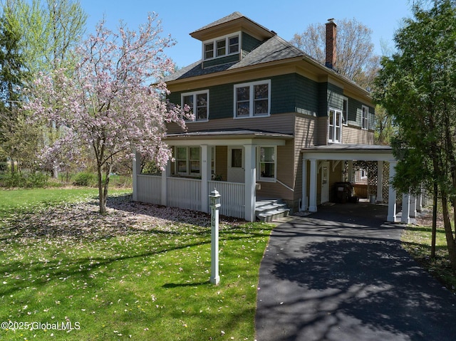 traditional style home with covered porch, asphalt driveway, a chimney, a front yard, and a carport