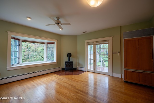 spare room with a baseboard heating unit, a wood stove, wood finished floors, and a ceiling fan