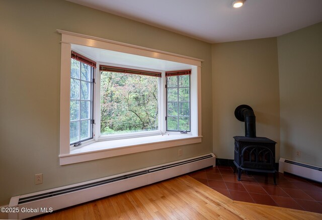unfurnished living room featuring baseboard heating, plenty of natural light, and a wood stove