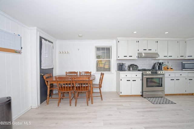 kitchen with under cabinet range hood, appliances with stainless steel finishes, tasteful backsplash, and light wood-style floors