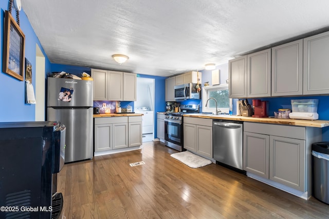 kitchen with wooden counters, gray cabinetry, stainless steel appliances, dark wood-type flooring, and washer / dryer