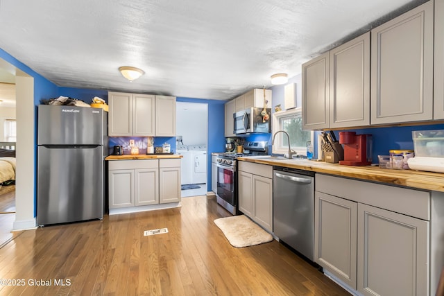 kitchen with separate washer and dryer, butcher block countertops, appliances with stainless steel finishes, a sink, and light wood-type flooring