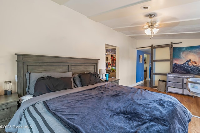 bedroom with wood finished floors, a barn door, baseboards, and a walk in closet
