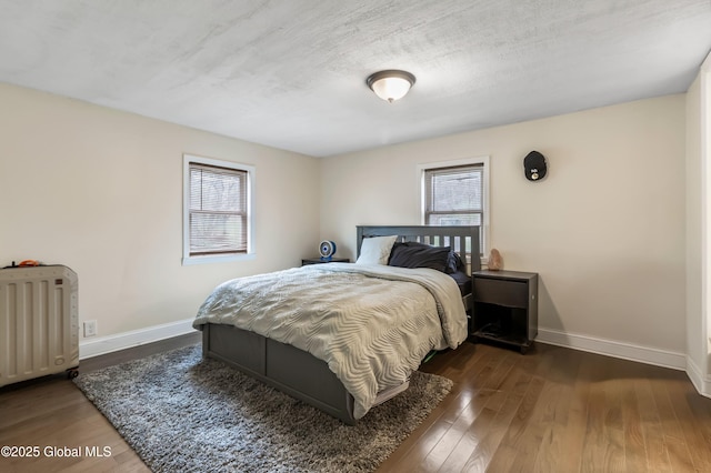 bedroom featuring radiator, multiple windows, wood finished floors, and baseboards