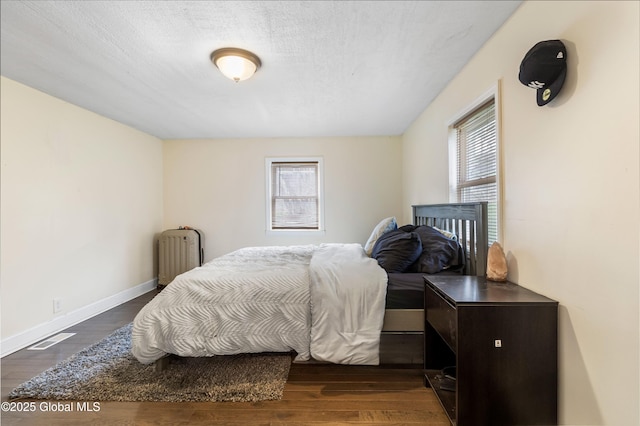 bedroom with dark wood-type flooring, visible vents, radiator heating unit, and baseboards