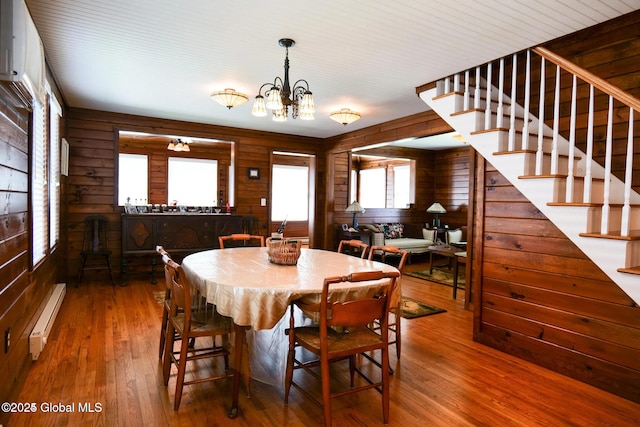 dining space with wooden walls, an inviting chandelier, hardwood / wood-style floors, a baseboard heating unit, and stairway