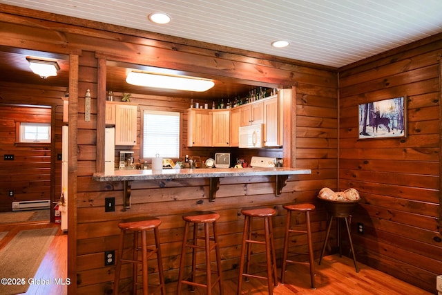 kitchen with wooden walls, white appliances, a wealth of natural light, wood finished floors, and a baseboard radiator