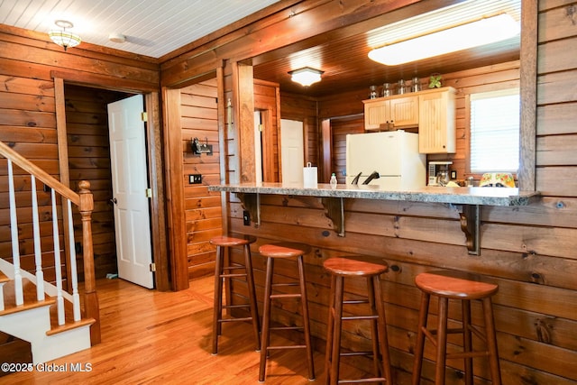 kitchen featuring wooden walls, light brown cabinetry, a kitchen breakfast bar, freestanding refrigerator, and light wood-type flooring