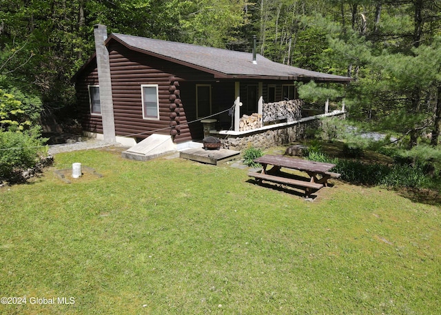 rear view of house featuring a chimney, log exterior, a forest view, and a yard