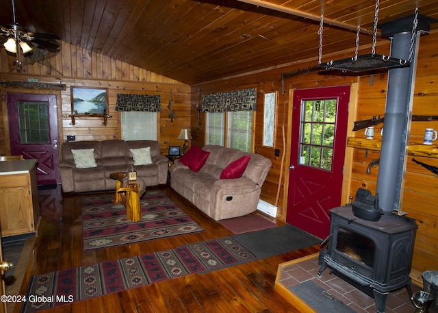 living area featuring lofted ceiling, dark wood-style flooring, wood walls, and a wood stove
