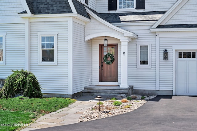 view of exterior entry featuring a shingled roof and a garage