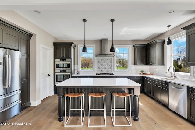 kitchen featuring a sink, a kitchen breakfast bar, wall chimney range hood, stainless steel appliances, and light wood-type flooring