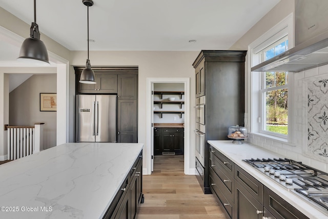 kitchen featuring pendant lighting, extractor fan, light wood-type flooring, appliances with stainless steel finishes, and light stone counters
