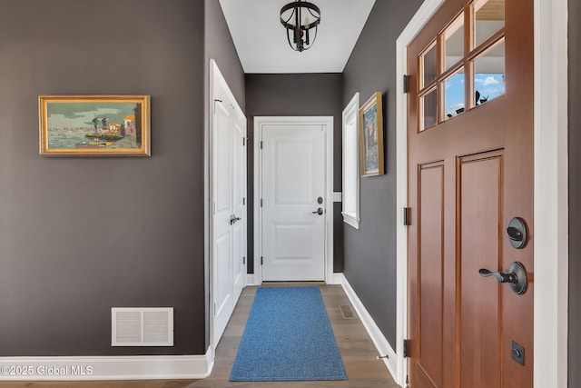 doorway with baseboards, visible vents, and wood finished floors