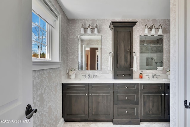full bath with double vanity, wallpapered walls, a shower stall, and a sink