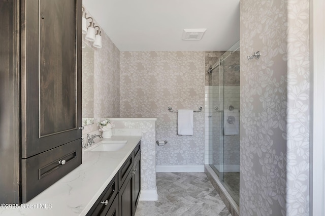 bathroom with a stall shower, wallpapered walls, visible vents, baseboards, and vanity