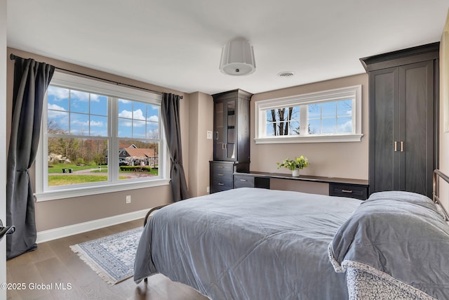 bedroom featuring wood finished floors, baseboards, visible vents, and multiple windows