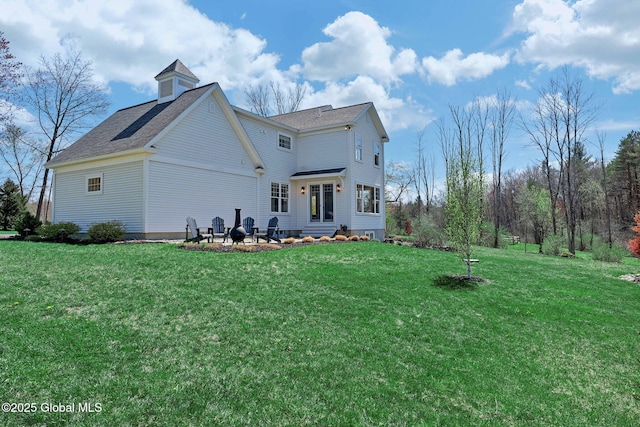 rear view of property with roof with shingles, entry steps, and a lawn