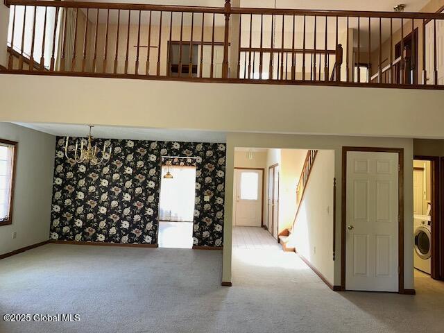 unfurnished living room with washer / dryer, baseboards, a high ceiling, and carpet